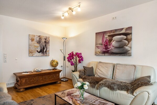A living room with a sofa, a wooden sideboard, a globe, and a painting of stacked stones.
