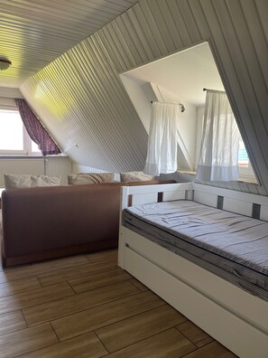 Un dormitorio con techo inclinado, una cama, un sofá y un ventanal con cortinas.