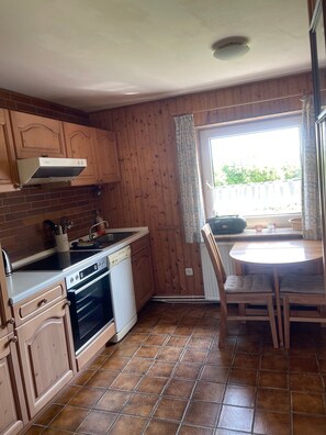 Una cocina con armarios de madera, estufa, lavavajillas y una mesa de comedor con sillas.