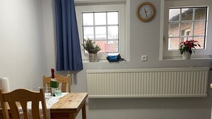 Un comedor con una mesa, sillas, una cortina azul, un reloj y plantas en macetas.