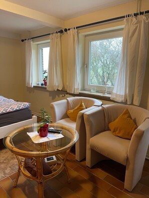 Une pièce comprenant un lit, deux chaises, une table ronde et une fenêtre avec des rideaux.