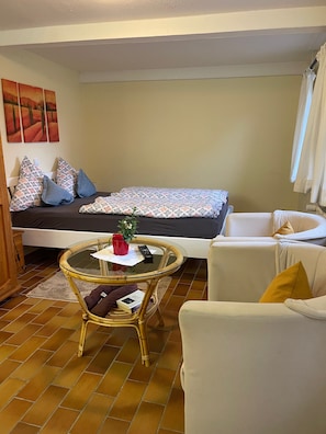 Una habitación acogedora con una cama, una mesita redonda pequeña, una silla y un sofá.