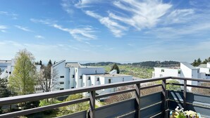 Et boligområde med moderne hvide bygninger, en klar blå himmel og et fjerntliggende skovlandskab.