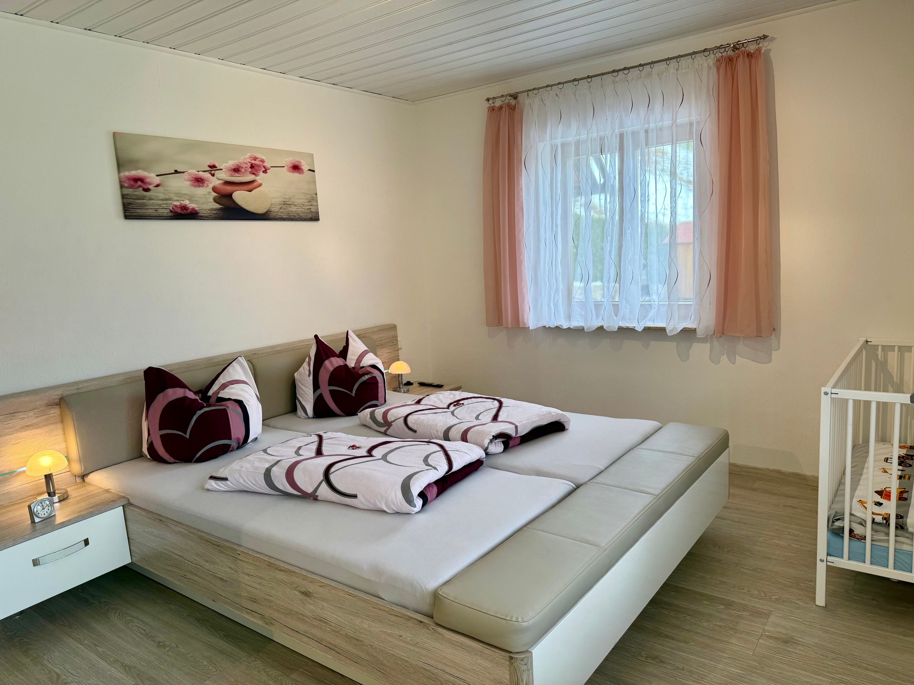 A bedroom with a bed, bedside table, lamp, and a crib.
