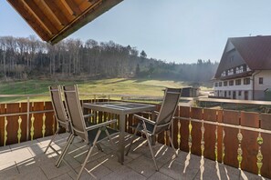 Un balcon avec une table et des chaises, donnant sur un paysage boisé et un bâtiment.