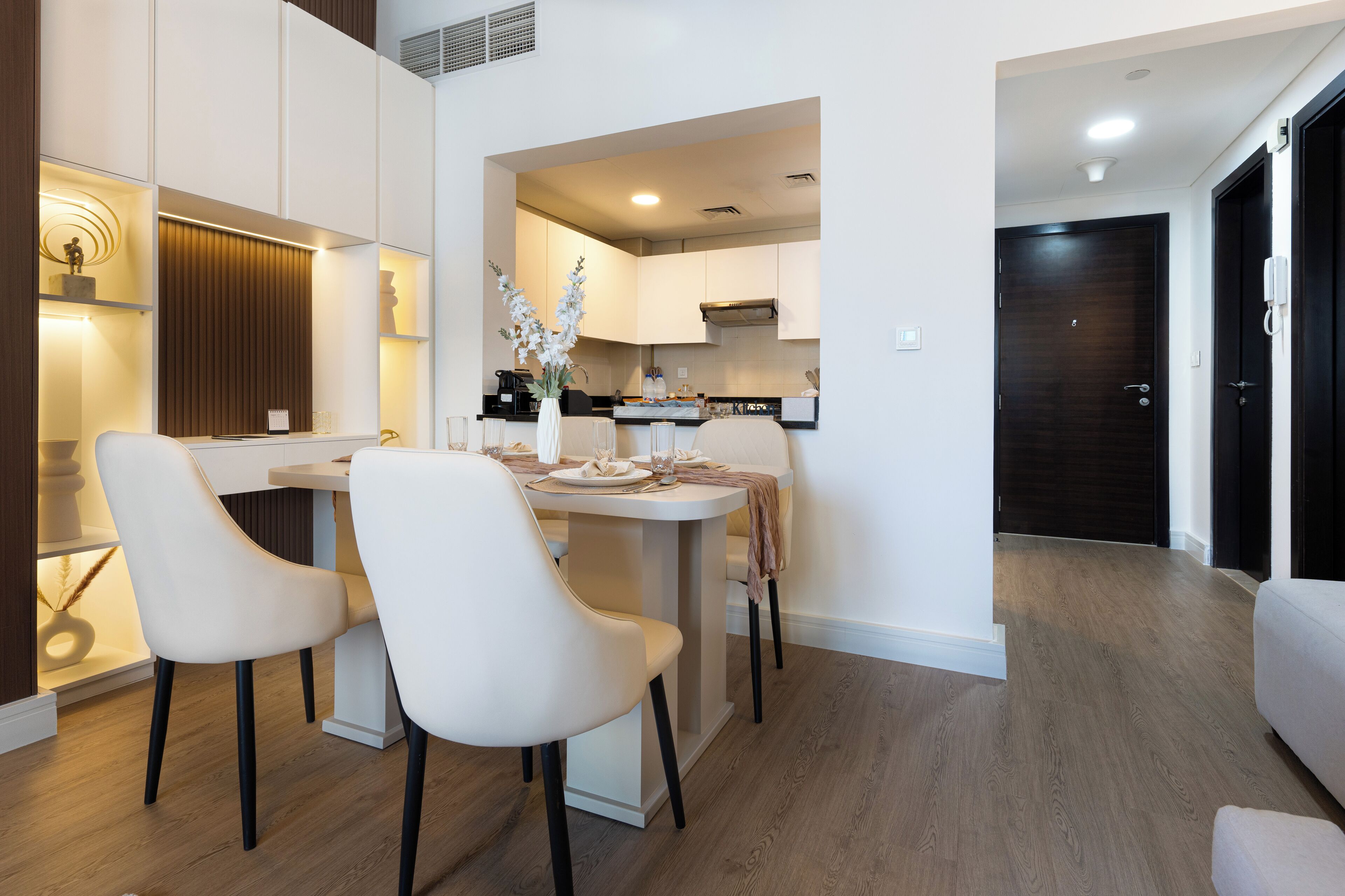 Une cuisine moderne avec des meubles blancs, un coin repas avec deux chaises blanches et un plancher en bois.