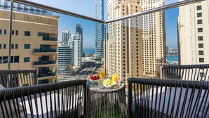 A balcony with wicker furniture, a table with fruits and a glass of orange juice, and a cityscape view. - Dubaiashome - Luxury Special Stay (Dubai)