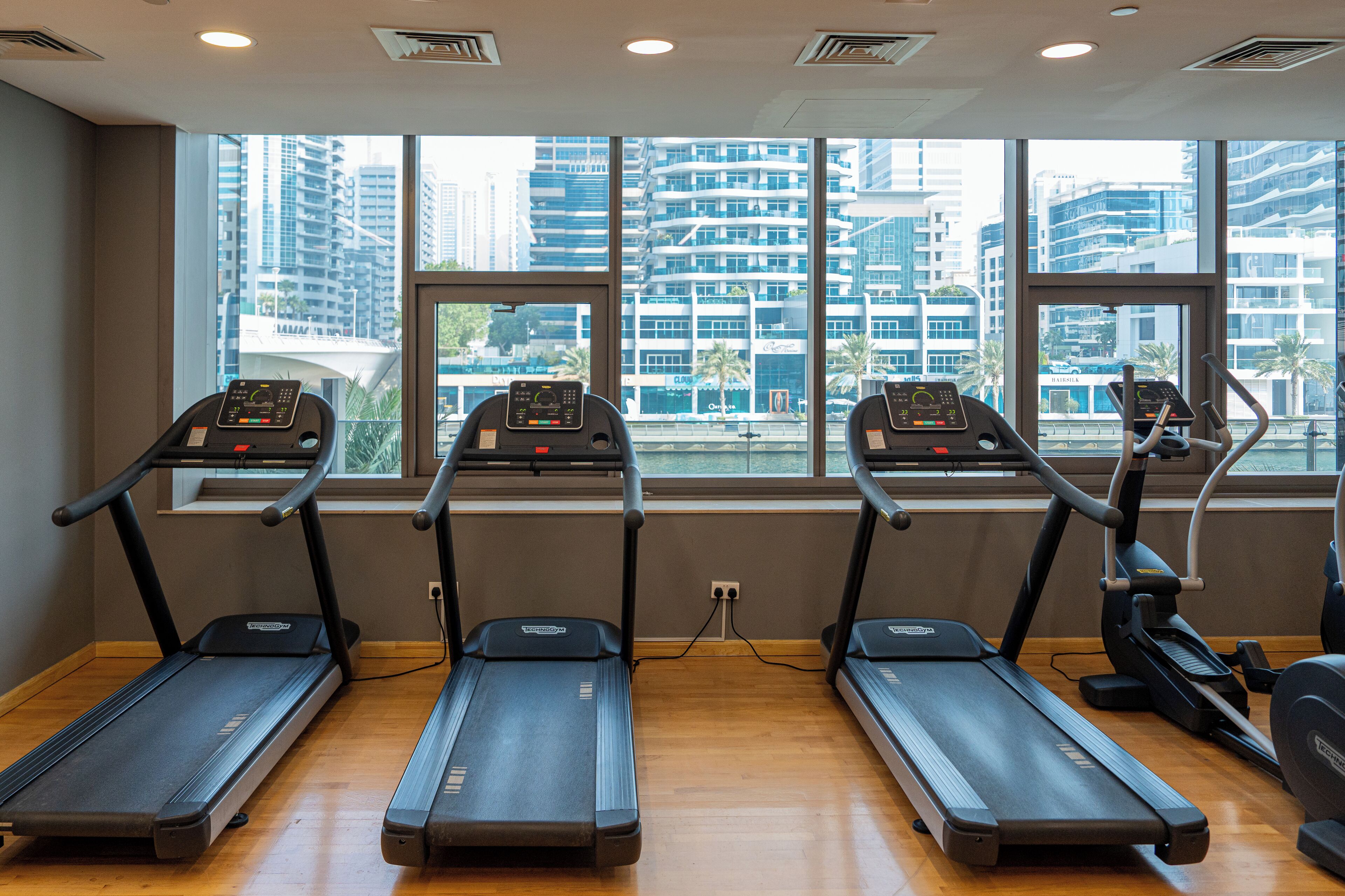A gym with treadmills and an exercise bike, large windows with a city view.