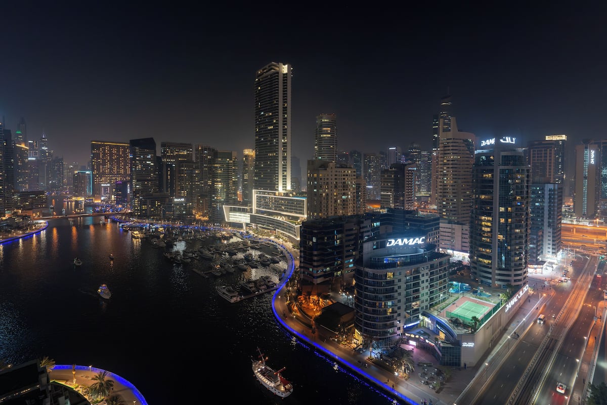 A nighttime cityscape with high-rise buildings, a marina, and a brightly lit hotel.