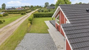 Ein rotes Gebäude mit einem grauen Dach, einer Schotterauffahrt und einem gepflegten Rasen.