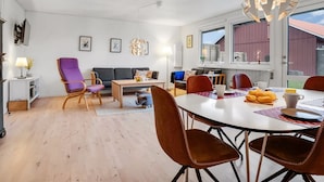 Een moderne woonkamer met een bank, een paarse fauteuil, een eettafel met stoelen, en een unieke bolvormige lamp.