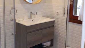 Ein Badezimmer mit weißem Waschbecken, einem Spiegel mit goldener Rahmung, einer Toilette und einer Duschkabine.