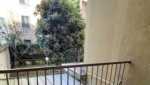 Ein Balkon mit Tisch für zwei Personen, einem Stuhl und Blick auf ein Gebäude und Bäume.