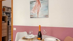 Ein Essbereich mit einem Tisch für zwei Personen, einer Champagnerflasche und einem Gemälde einer Frau am Meer an der Wand.
