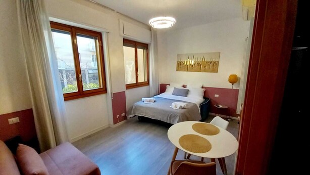 Ein Schlafzimmer mit Bett, Nachttischen, einem kleinen Tisch mit Stühlen, einem Fenster und einem Bild an der Wand.