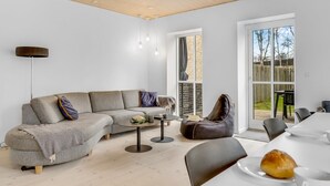 Un saló modern amb un sofà modular, una taula de centre rodona, un otomà de cuir i una zona de menjador amb taula i cadires.
