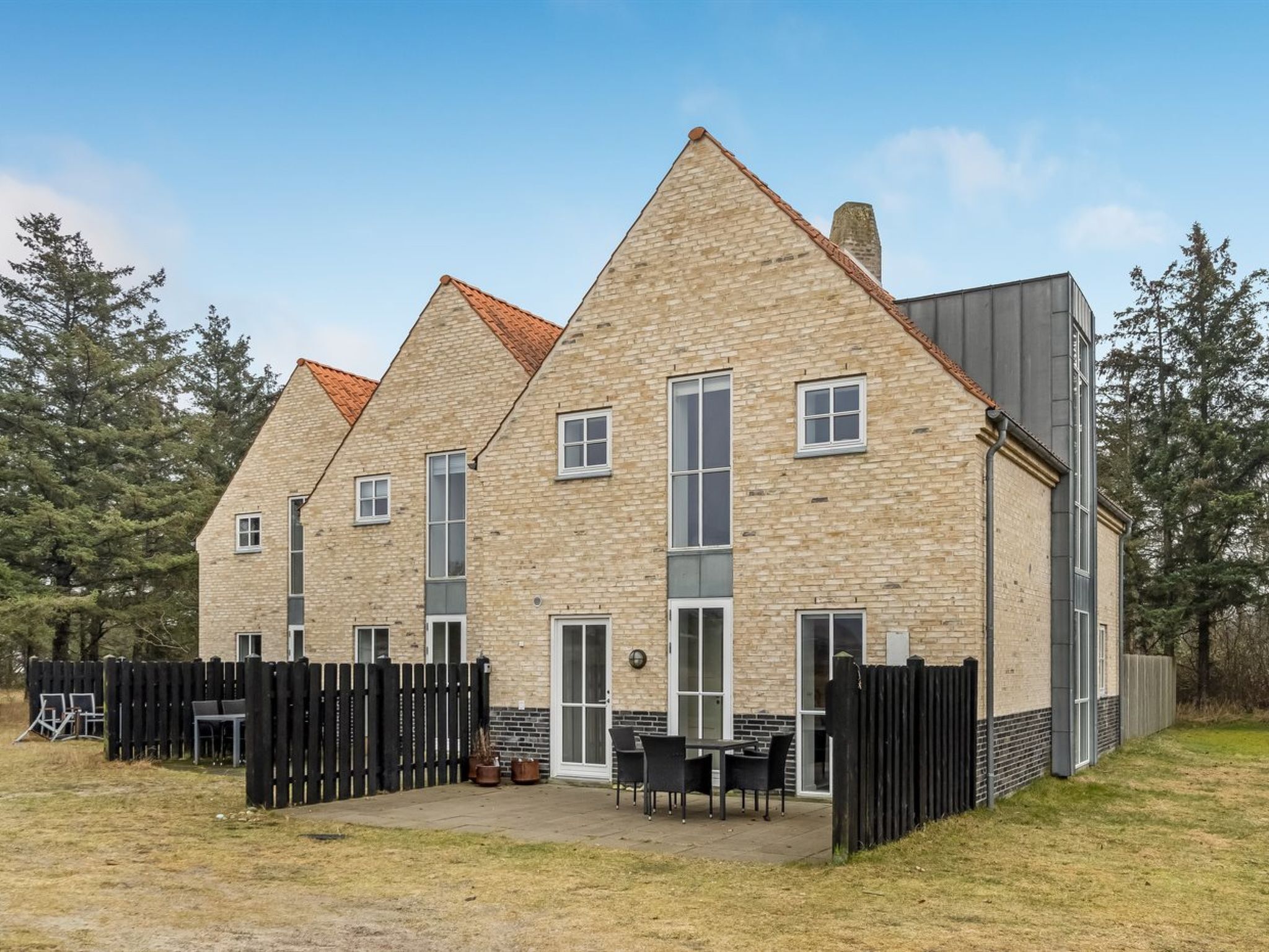 Il s’agit d’un bâtiment moderne avec une façade en briques et un toit en pente. Il est doté de nombreuses fenêtres et d’une grande porte, et un espace extérieur clôturé abrite des tables et des chaises.