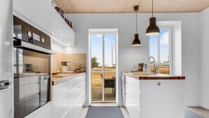 Una cuina moderna amb armaris blancs, forn integrat i una finestra gran amb vistes a l'exterior.