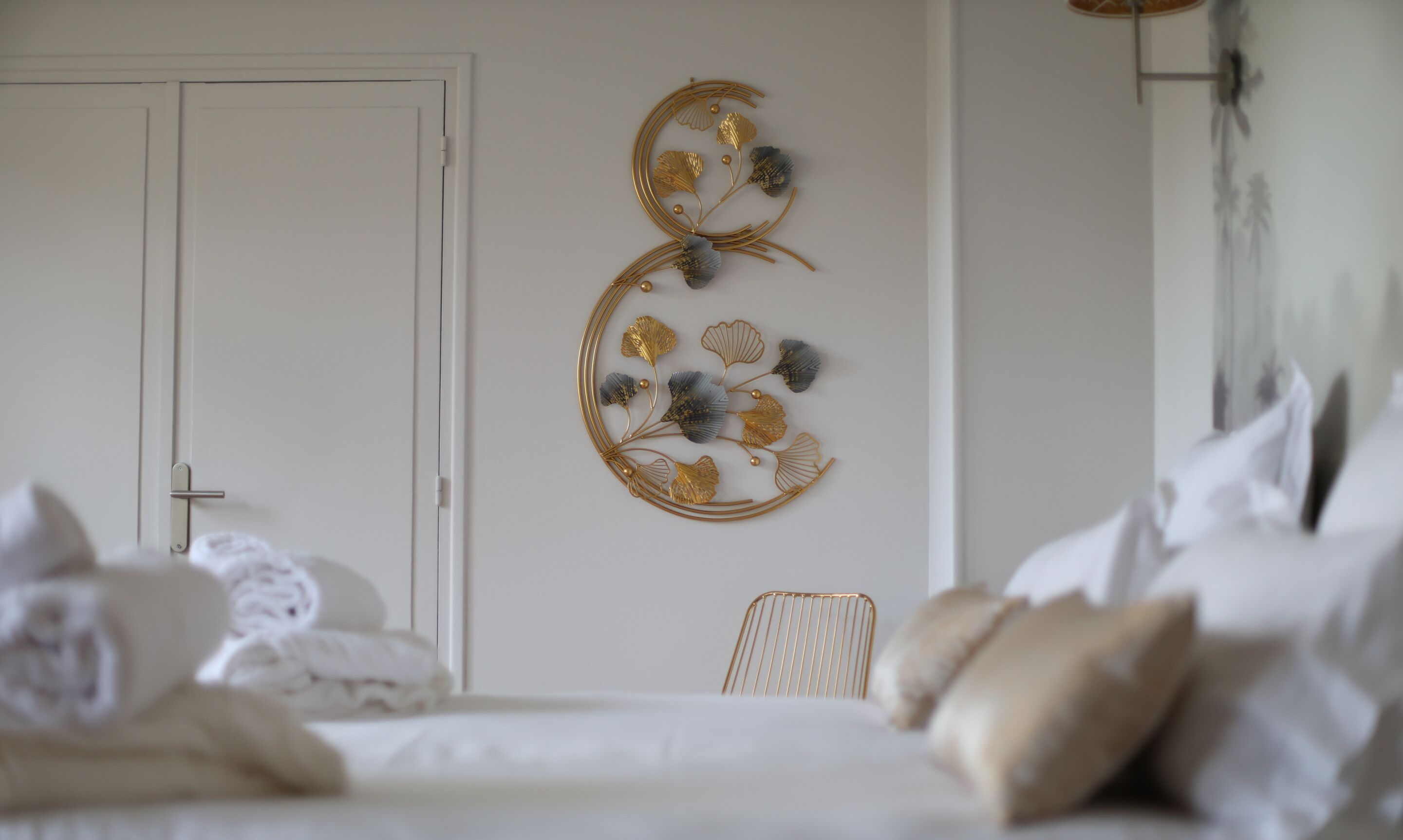 A bedroom with a bed, pillows, a chair, and a decorative wall piece.