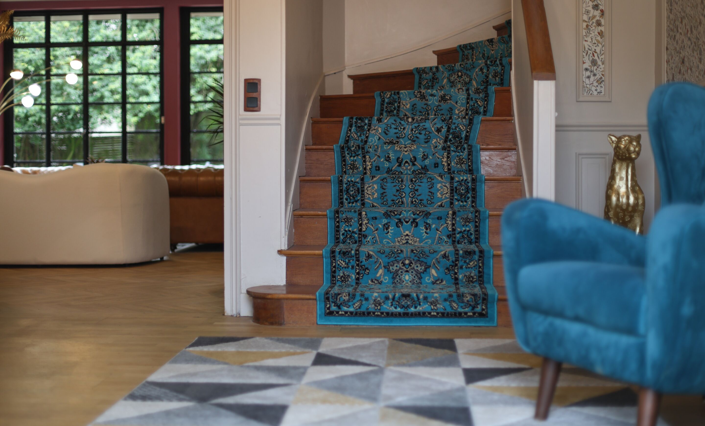 A staircase with a patterned carpet, a blue armchair, and a geometric rug.