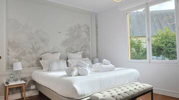 A bedroom with a large bed, bedside tables, a bench, and a window with a view of greenery.