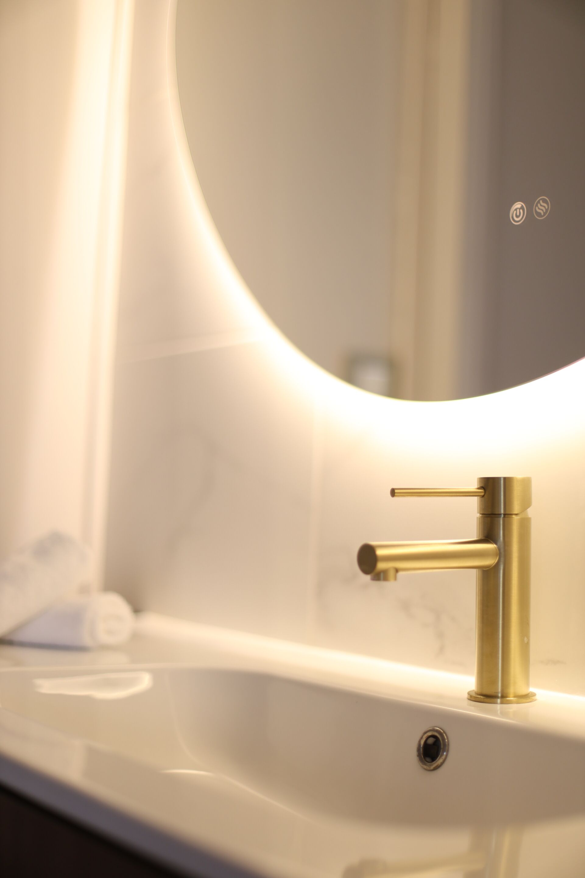 A bathroom with a white sink, a gold faucet, and a mirror.