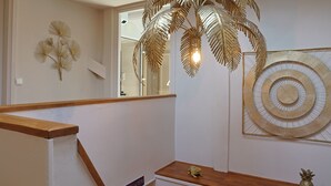 A staircase with a wooden handrail, a wall-mounted decorative palm leaf chandelier, and a framed circular artwork.