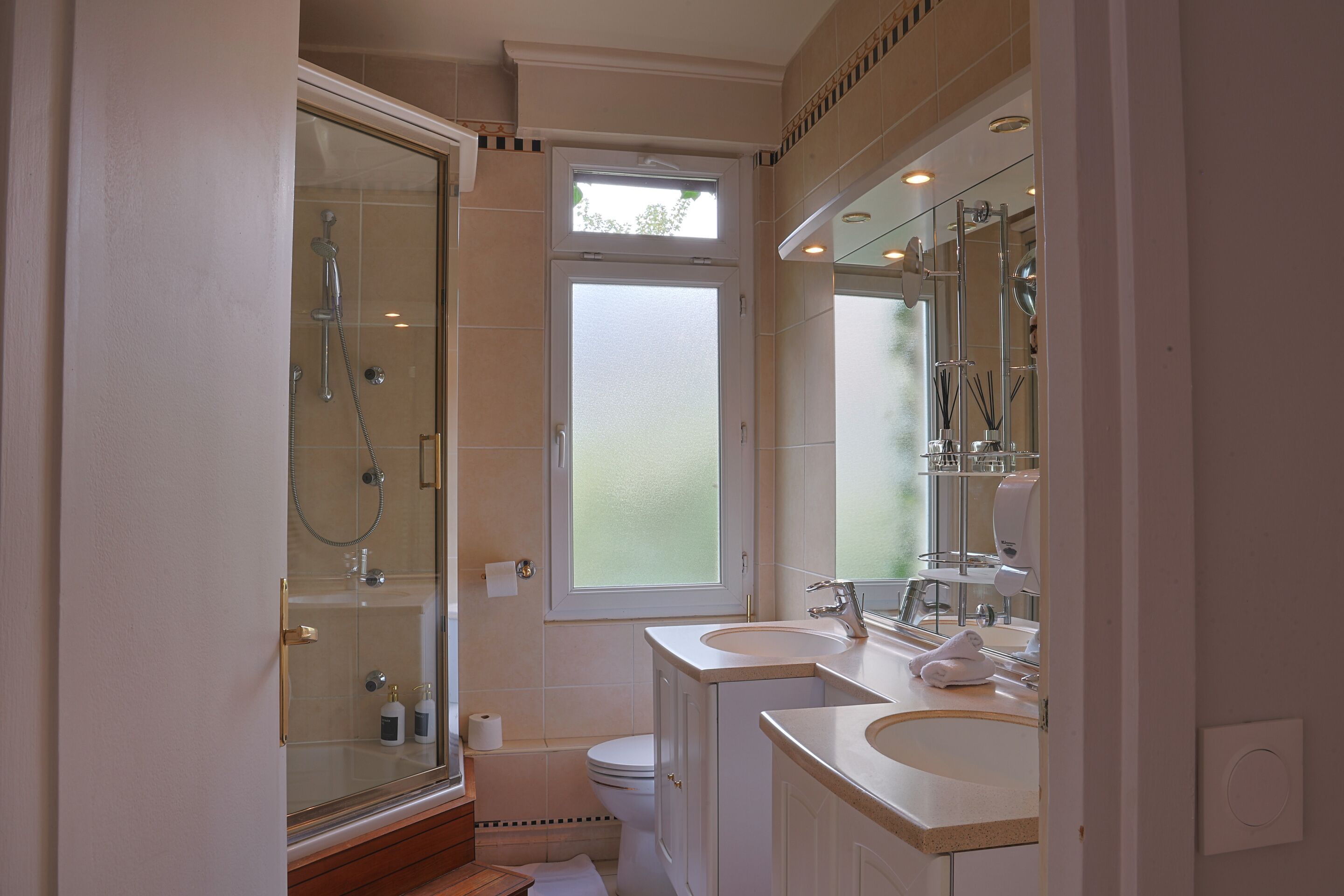 A bathroom with a glass-enclosed shower, a toilet, and two sinks with mirrors.