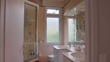 Une salle de bain avec une douche à parois de verre, des toilettes et deux lavabos avec miroirs.