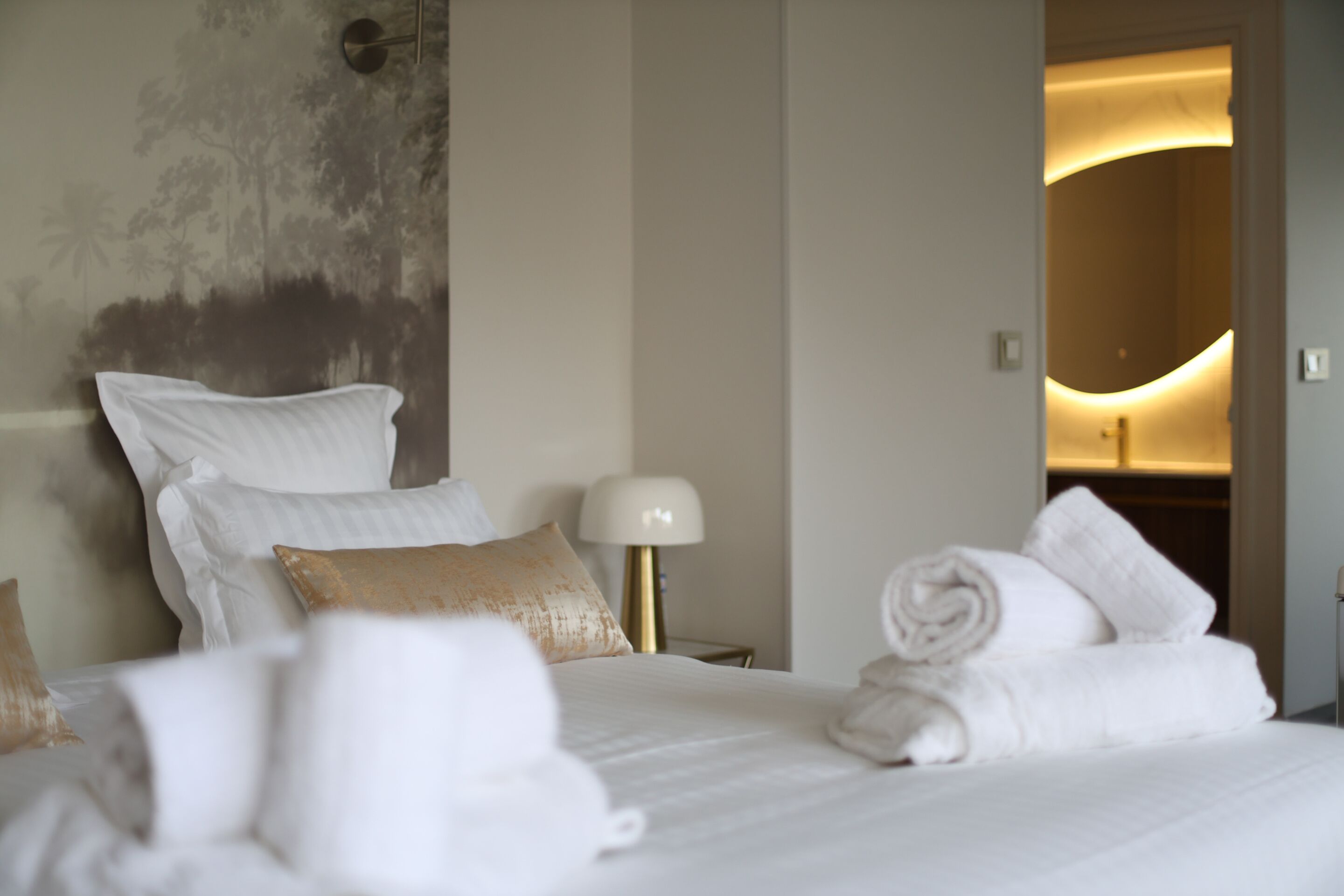 A hotel room with a bed, pillows, a lamp, and a towel rack.