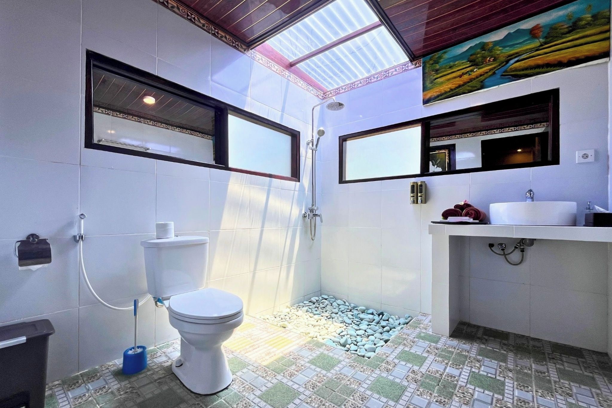 Un baño con inodoro, ducha y lavamanos, suelo de baldosas y tragaluz.