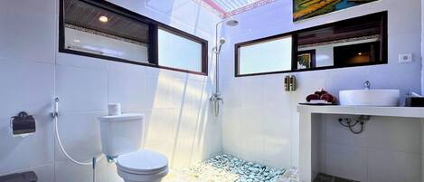 Un baño con inodoro, ducha y lavamanos, suelo de baldosas y tragaluz.