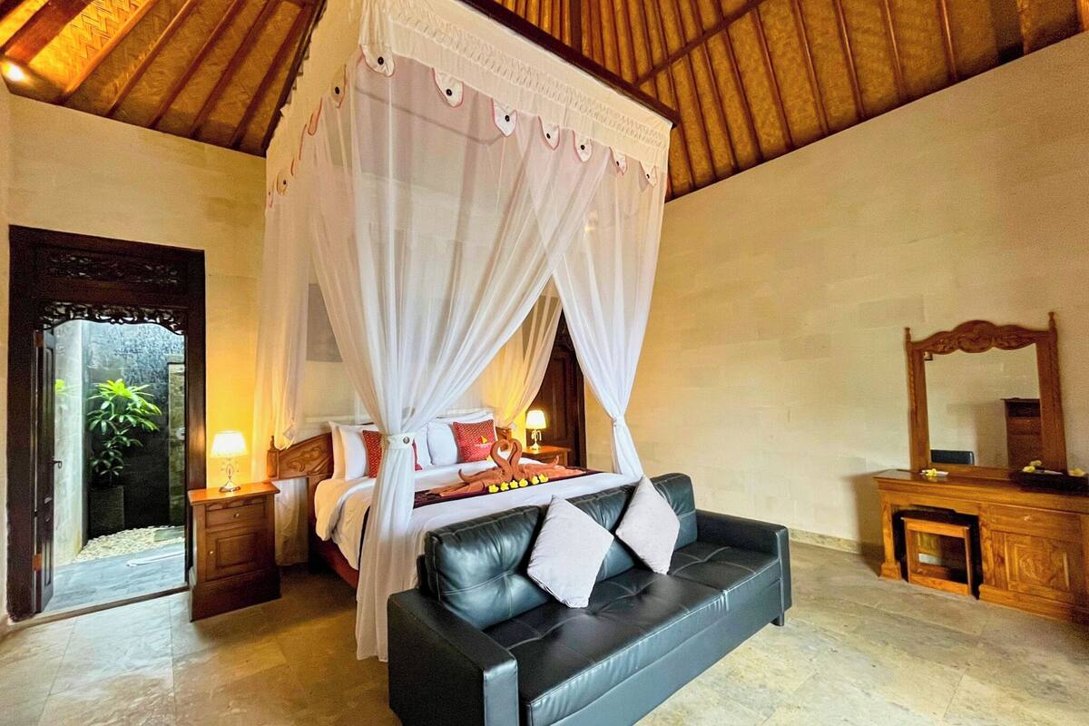 Une chambre à coucher avec un lit à baldaquin, un canapé en cuir noir, une table de chevet en bois et une commode en bois.