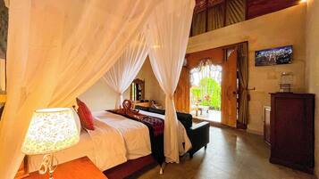A bedroom with a canopy bed, a bedside lamp, a wooden desk, and a TV on the wall.