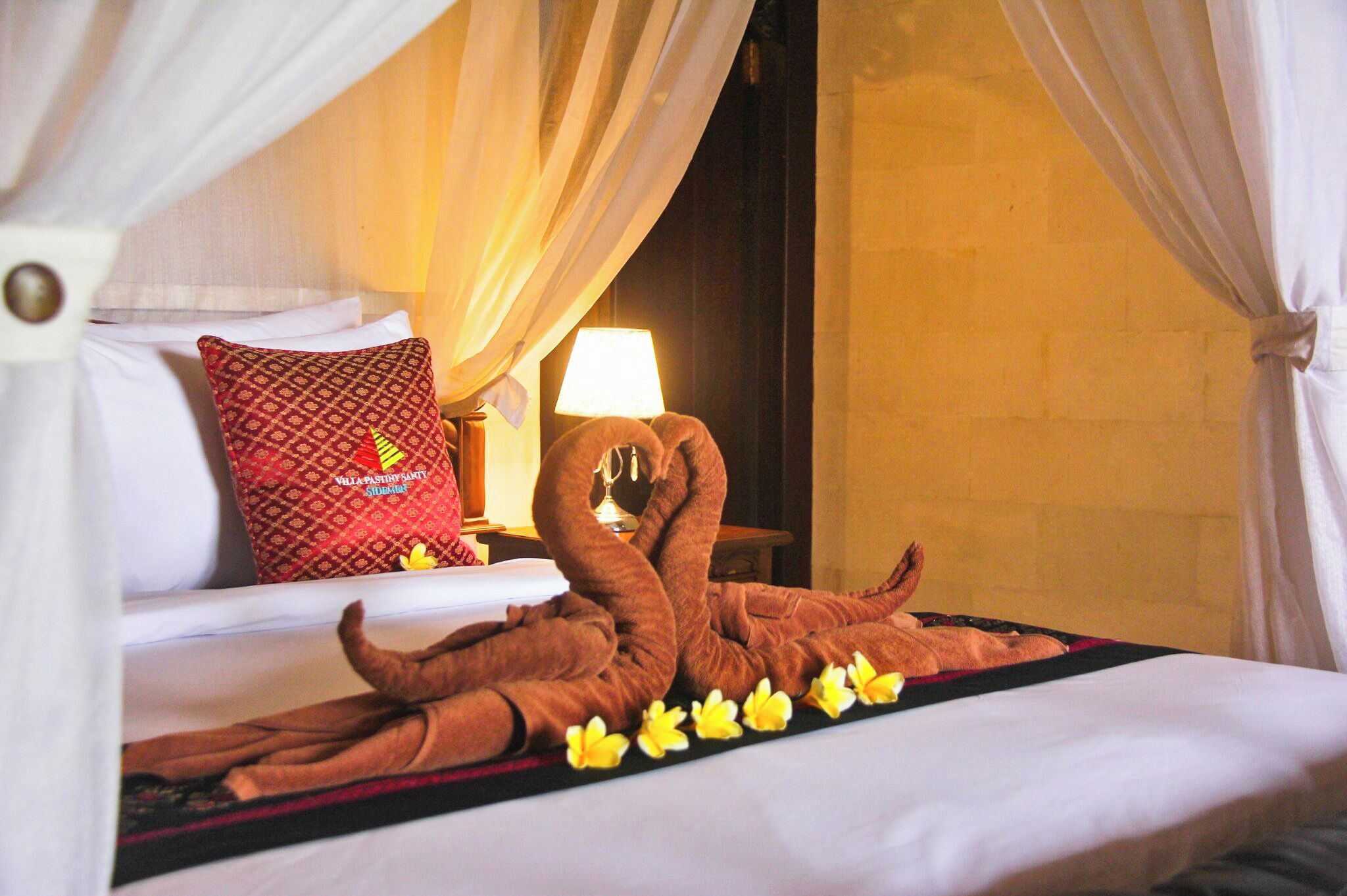 A bed with a decorative towel arrangement, a pillow, and a bedside lamp.