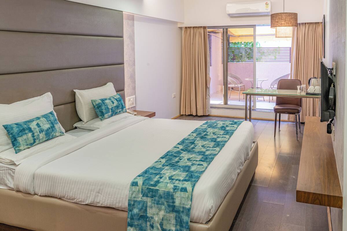 A hotel room with a large bed, a desk, a chair, and a TV.