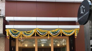 A building with a large glass entrance, a sign with 'DG' and 'Danish Grandur' on it, and a decorative garland above the entrance. - Hotel Dakshin Grandeur (Navi Mumbai)