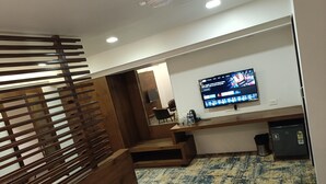 A hotel room with a TV, a desk, a bed, and a patterned rug. - Hotel Dakshin Grandeur (Navi Mumbai)