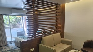 A modern room with a sofa, a small round table, and a wooden partition with horizontal slats. - Hotel Dakshin Grandeur (Navi Mumbai)
