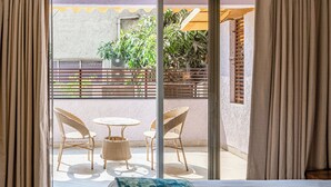 A hotel room with a bed, a view of an outdoor balcony with wicker chairs and a table, and a window with curtains. - Hotel Dakshin Grandeur (Navi Mumbai)