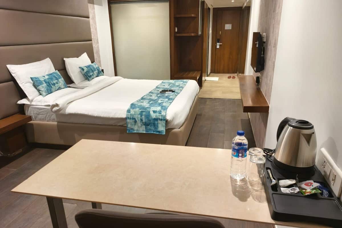 A hotel room with a bed, a bedside table with a kettle and cups, a water bottle, and a small table.