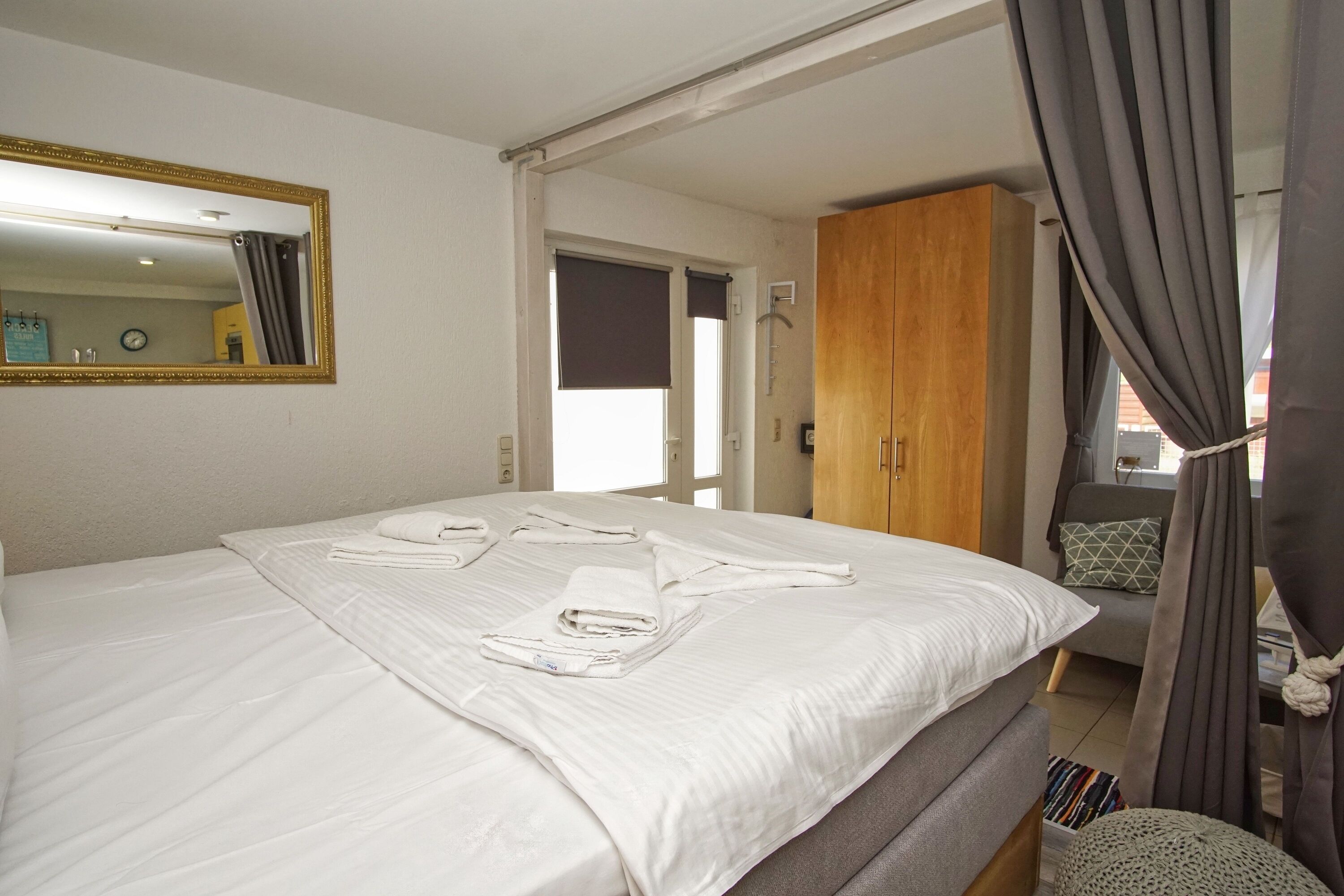 Un lit bien fait, avec du linge de lit et des serviettes blanches, une armoire en bois et un miroir au mur.