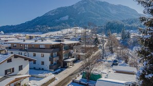 A modern building with multiple floors and balconies, surrounded by snow-covered streets and trees. - Apartment in Brixen im Thale With Parking (Brixen im Thale)