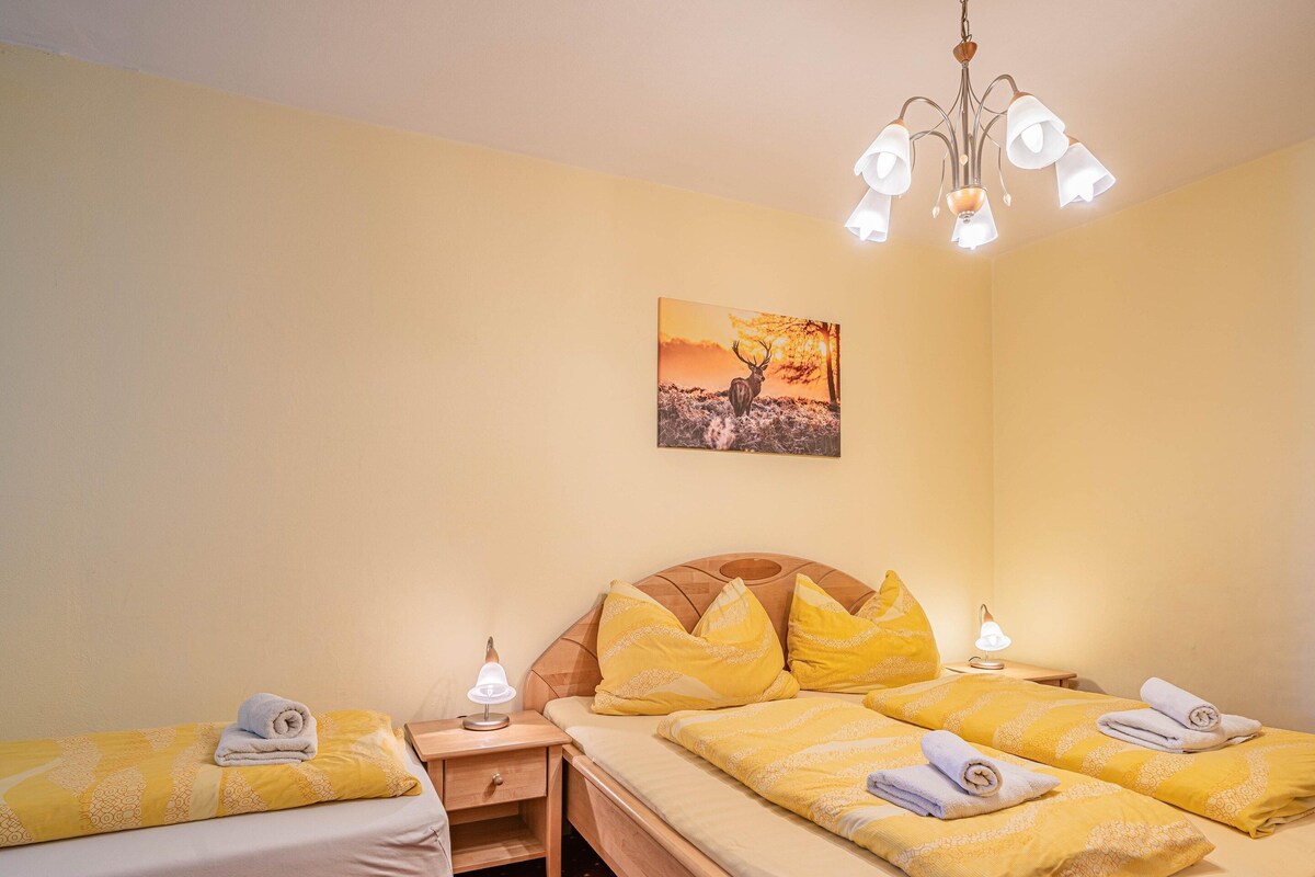 A hotel room with two beds, a wooden headboard, a nightstand with a lamp, and a painting on the wall.