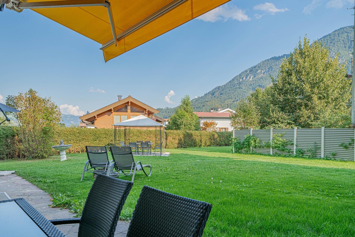 A patio with outdoor furniture, a yellow umbrella, and a view of a mountain and a house in the background.