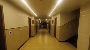 A long, well-lit hallway with doors on both sides, leading to a staircase at the end.