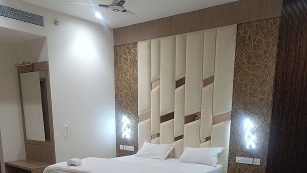 A modern hotel room with a large bed, a round table, a white chair, and a ceiling fan.