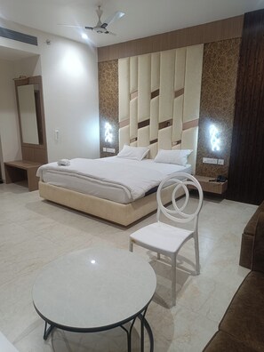 Una habitación de hotel moderna con una cama grande, una mesa redonda, una silla blanca y un ventilador de techo.