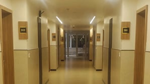 A hotel corridor with wooden doors, numbered room signs, and a tiled floor.