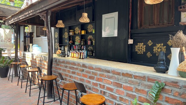 A bar area with brick walls, hanging wicker lamps, and a variety of bottles and decorative items on shelves. - La MaiSon Du laos Hotel (Luang Prabang)